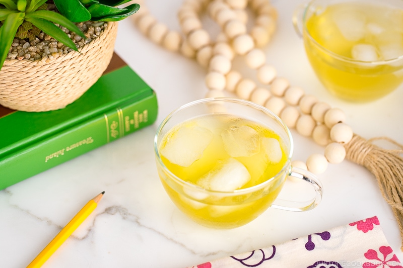 green iced tea in a glass cup on top of marble table next to a book and a plant