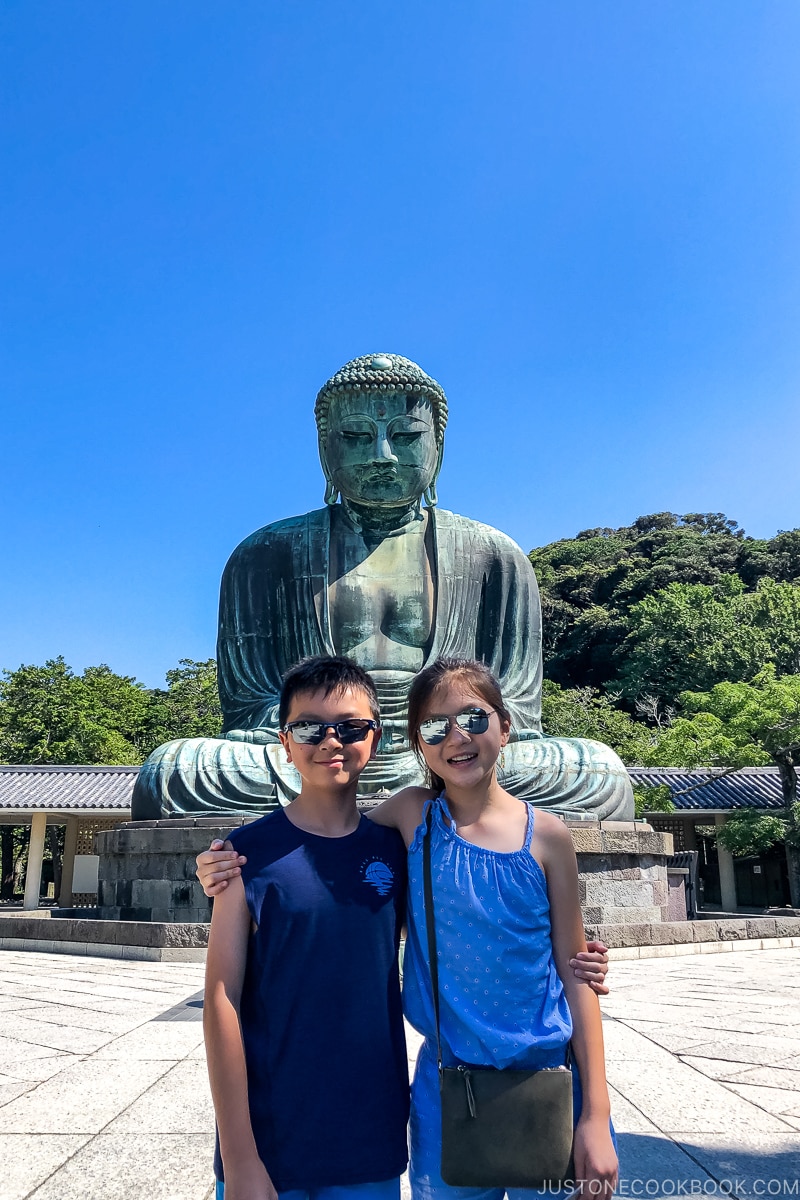 two children standing in front of a giant Buddha statue