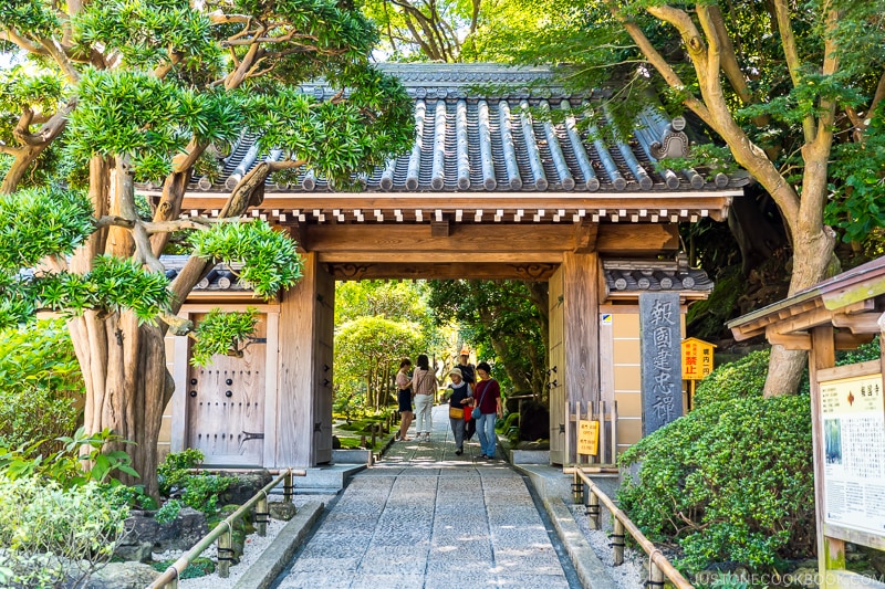 a wooden gate with tiled roof over a stone path
