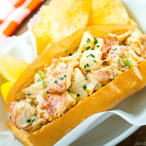 Lobster Roll served in a white dish along with potato chips and lemon.