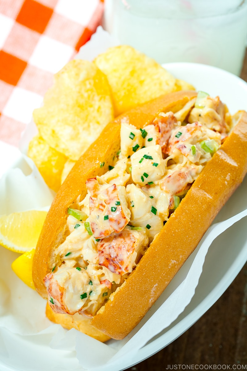 Lobster Roll served in a white dish along with potato chips and lemon.