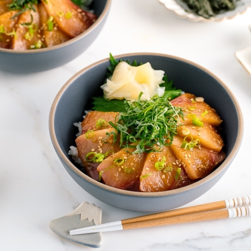 A ceramic bowl containing miso marinated hamachi served on bed of steamed rice along with shiso, scallion, and sushi ginger.