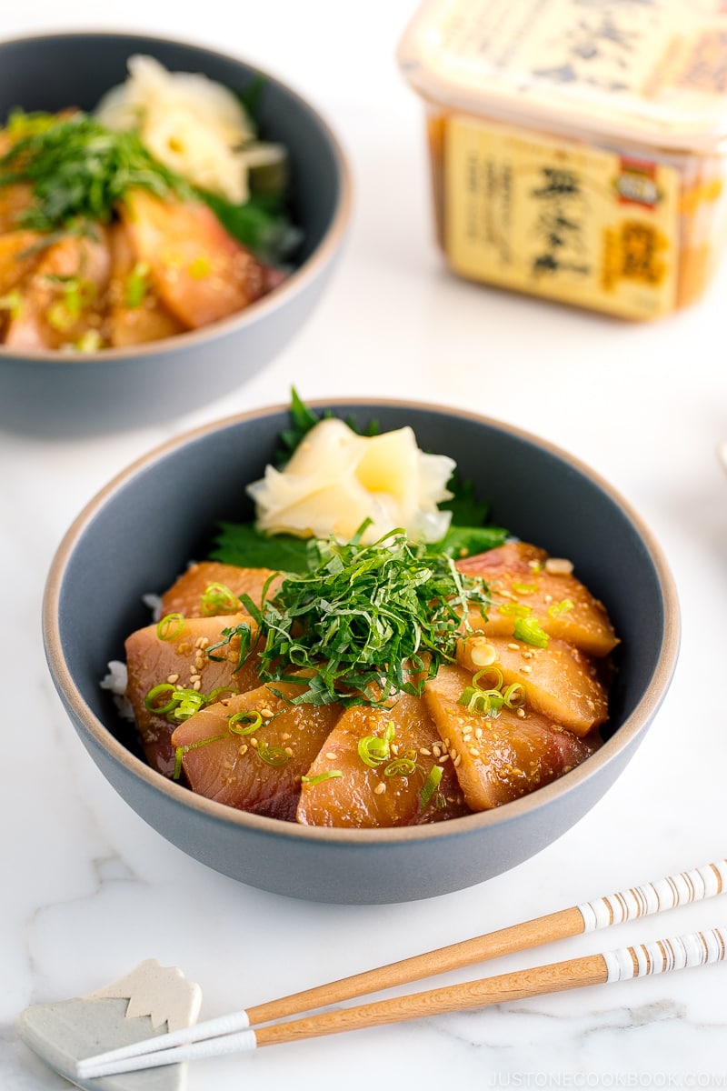 A ceramic bowl containing miso marinated hamachi served on bed of steamed rice along with shiso, scallion, and sushi ginger.