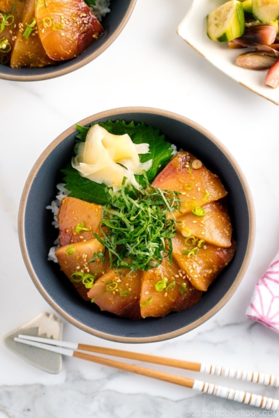 A ceramic bowl containing miso marinated hamachi served on bed of steamed rice along with shiso, scallion, and sushi ginger.