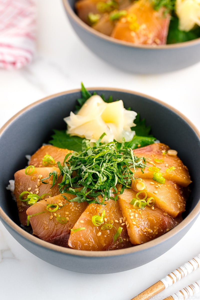 A ceramic bowl containing miso marinated hamachi served on bed of steamed rice along with shiso, scallion, and sushi ginger.