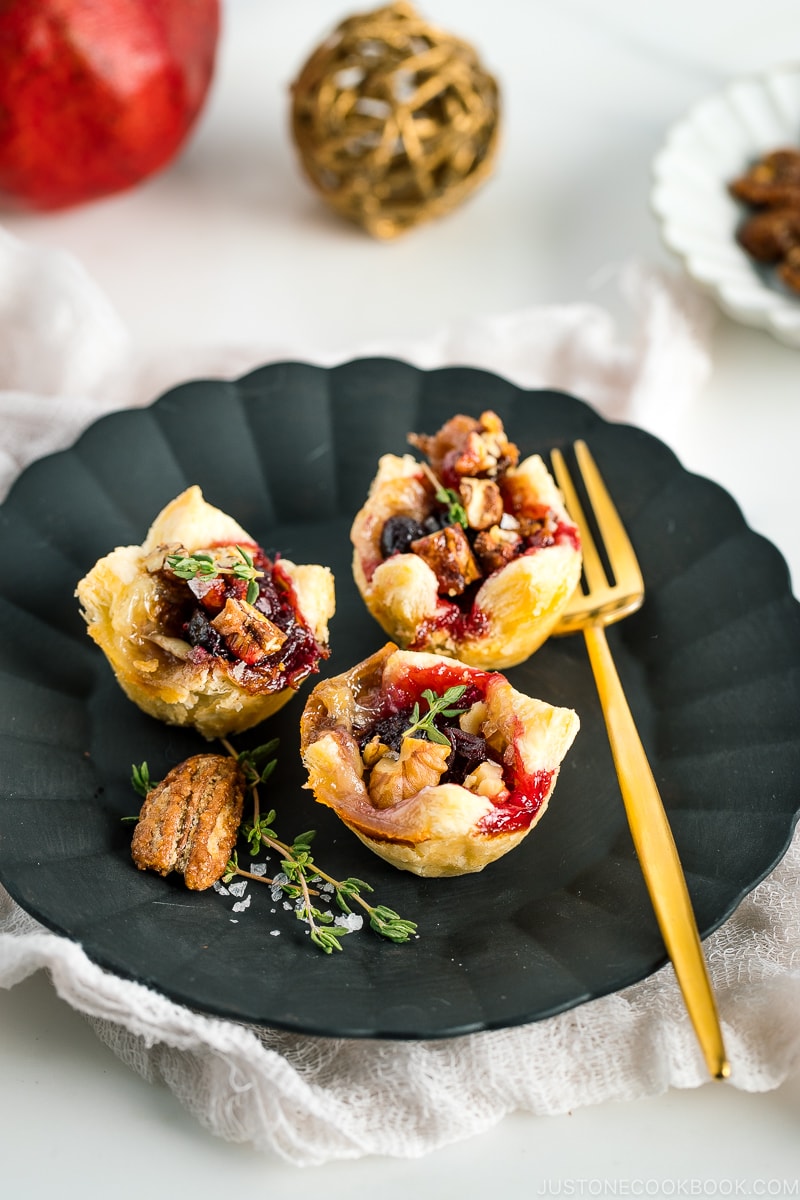 Cranberry Brie Bites placed on a black plate garnished with thyme, candied pecans and flake salt.
