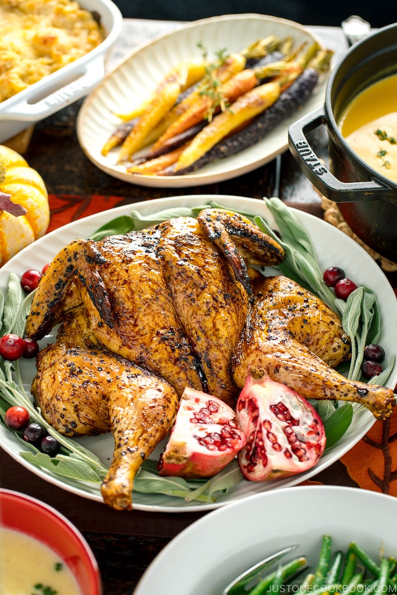 A white platter containing Honey Soy Glazed Spatchcock Chicken decorated with sage, pomegranate, and cranberries.