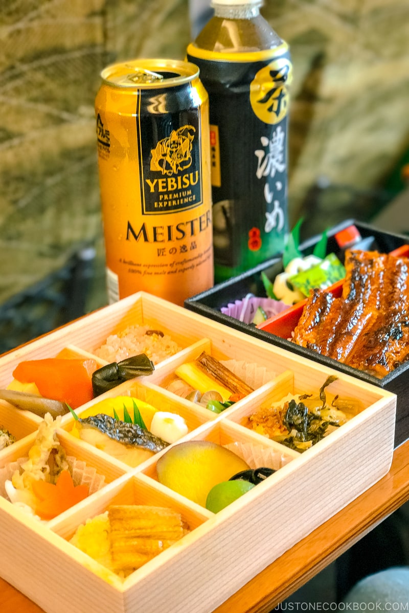 two bento boxes on a train table next to a beer can and tea bottle