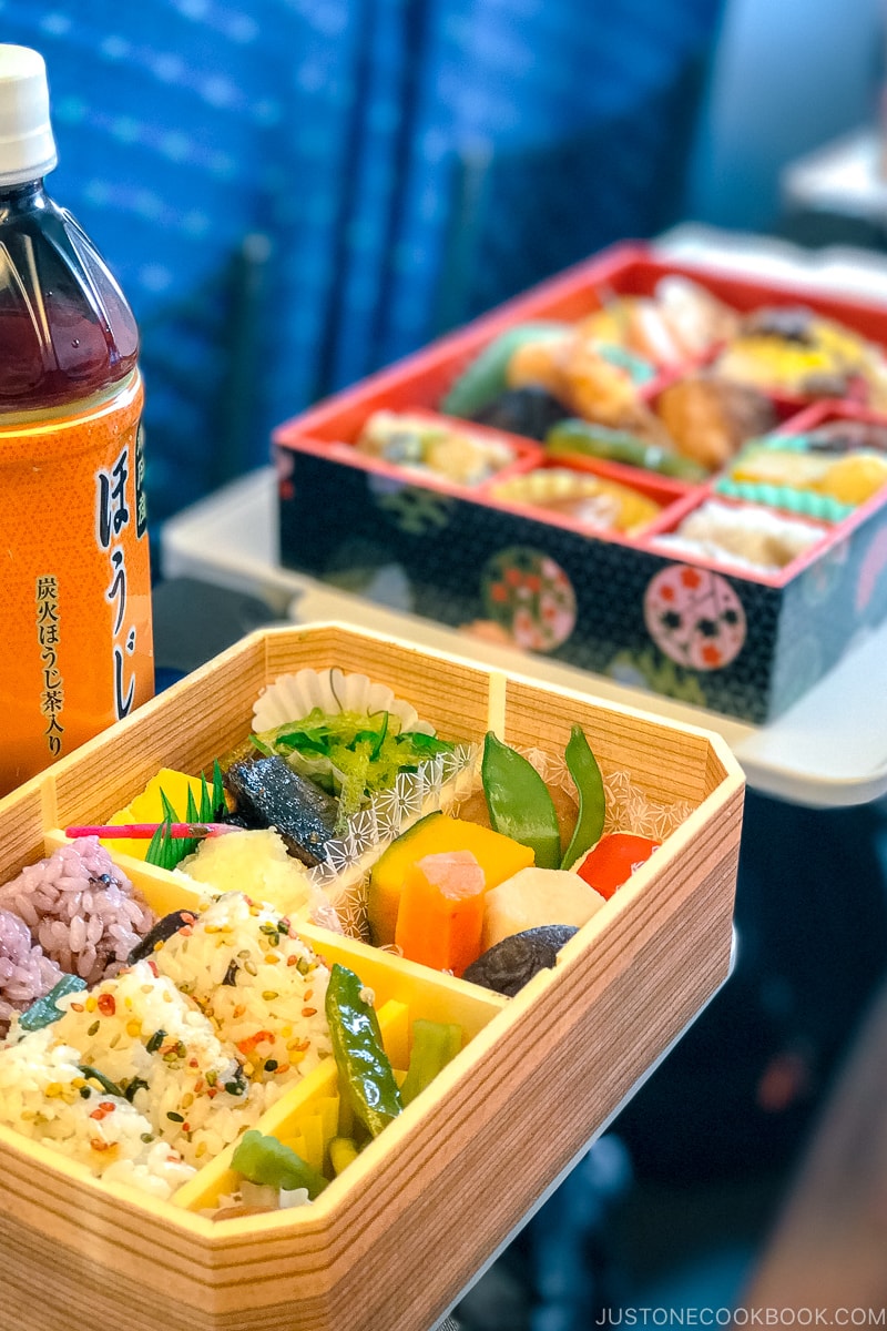 two bento boxes on a train table next to a bottle of tea