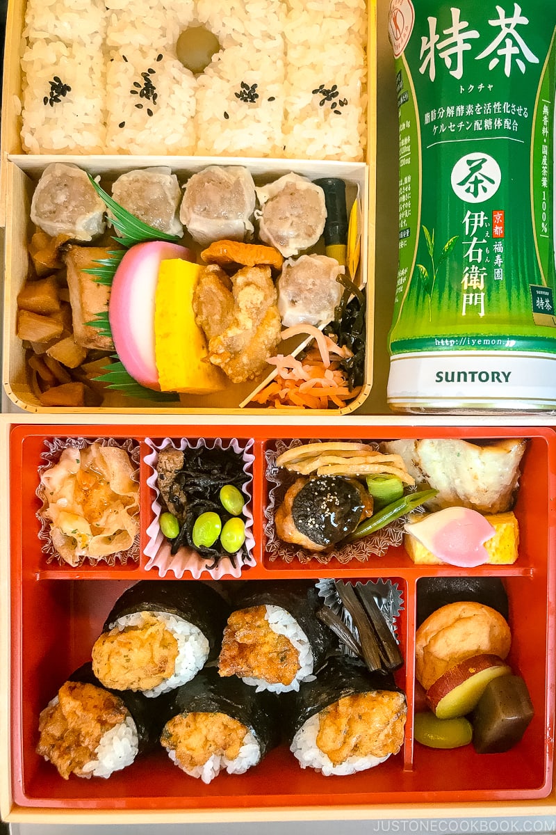 two bento boxes on a train table next to a bottle of tea