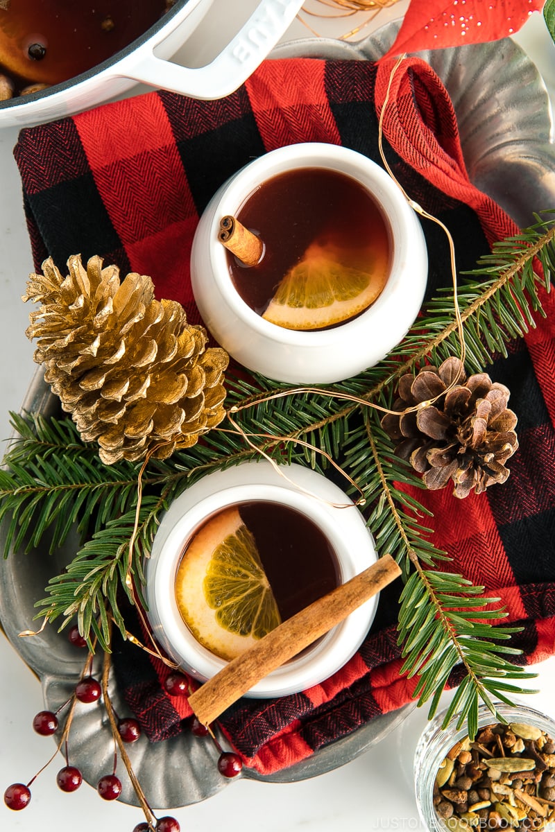 White cups containing hot mulled cider garnished with orange slice and a cinnamon stick.