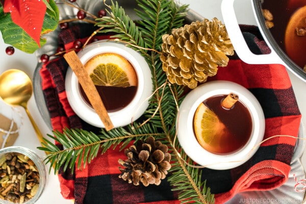 White cups containing hot mulled cider garnished with orange slice and a cinnamon stick.