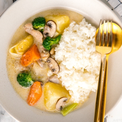 A beige ceramic dish containing steamed rice and Japanese cream stew.