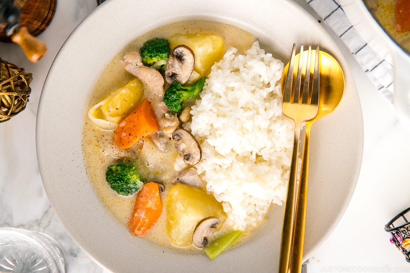 A beige ceramic dish containing steamed rice and Japanese cream stew.