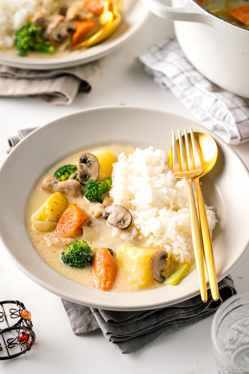 A beige ceramic dish containing steamed rice and Japanese cream stew.