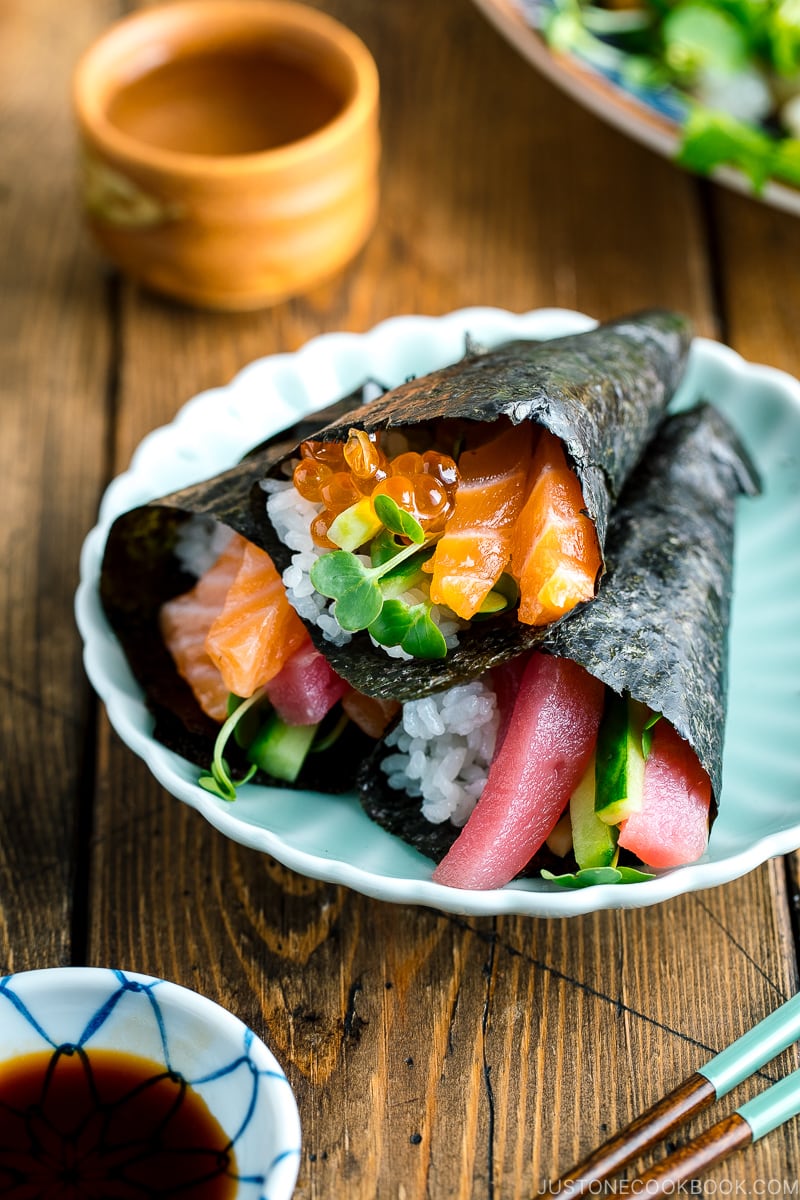 A light green plate containing three types of Temaki Sushi (Hand Roll Sushi) - salmon and tuna, salmon and ikura, and tuna and cucumber.