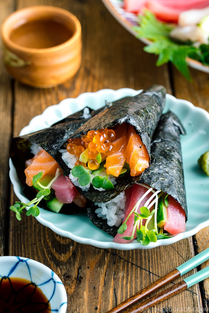 Un piatto verde chiaro contenente tre tipi di Temaki Sushi (Hand Roll Sushi): salmone e tonno, salmone e ikura e tonno e cetriolo.