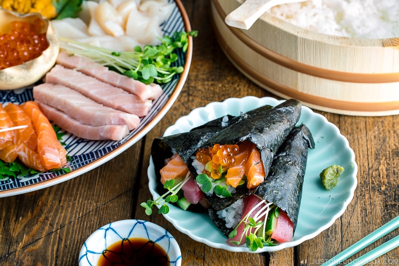 A light green plate containing three types of Temaki Sushi (Hand Roll Sushi) - salmon and tuna, salmon and ikura, and tuna and cucumber.