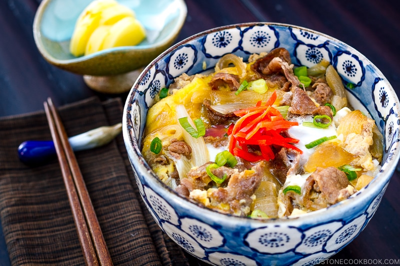 A bowl containing simmered beef, onion, and egg over steamed rice.