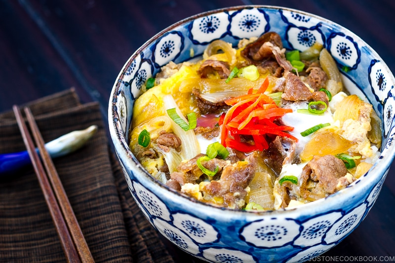 A bowl containing simmered beef, onion, and egg over steamed rice.