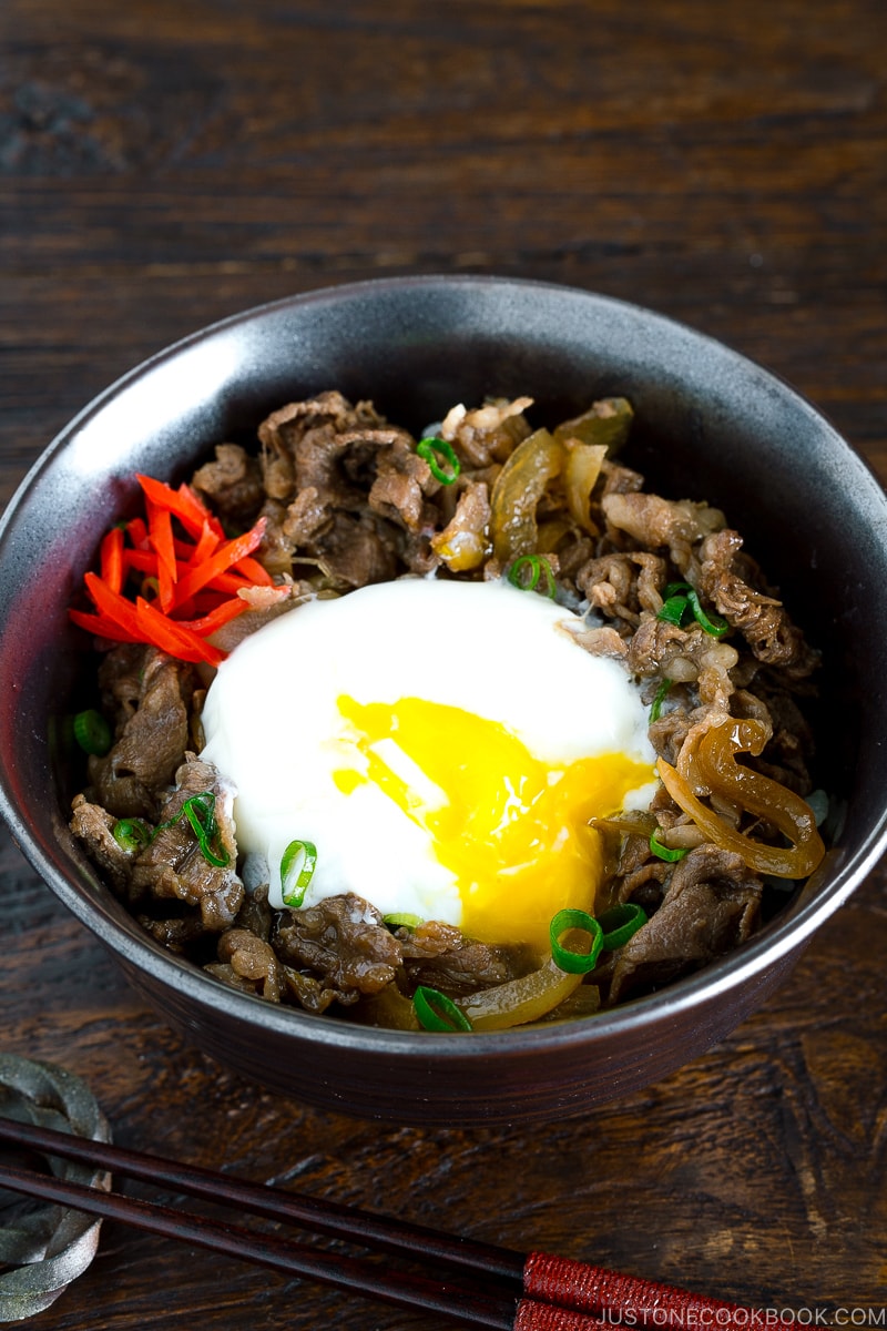 A bowl containing beef and egg over steamed rice.