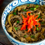 A bowl containing simmered beef over steamed rice.