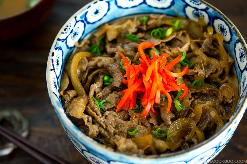 A bowl containing simmered beef over steamed rice.