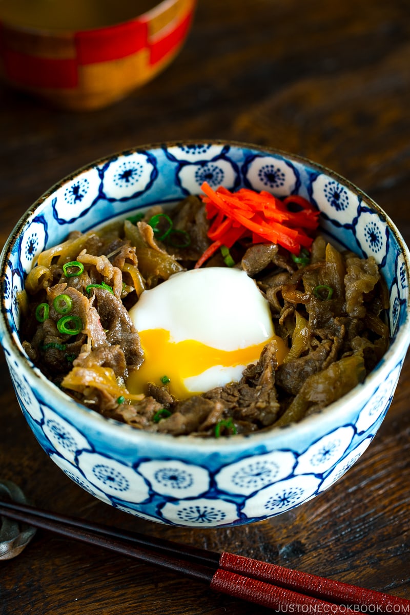 A bowl containing beef and egg over steamed rice.