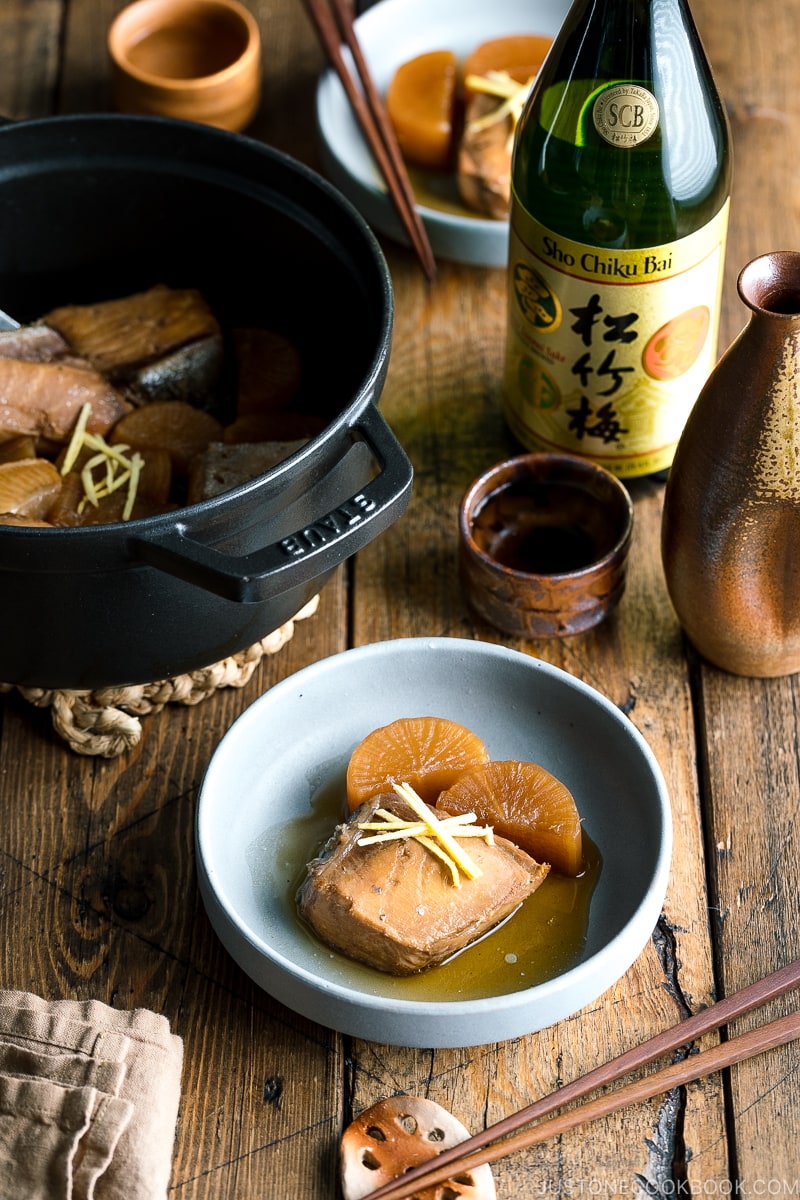 A grey bowl containing buri daikon, a simmered yellowtail and daikon radish, garnished with julienned ginger.