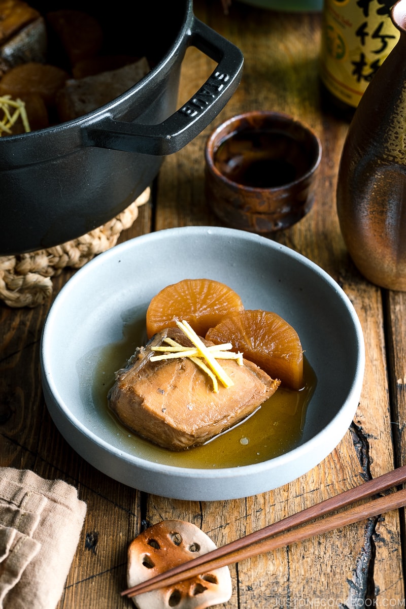 A grey bowl containing buri daikon, a simmered yellowtail and daikon radish, garnished with julienned ginger.