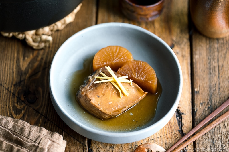 A grey bowl containing buri daikon, a simmered yellowtail and daikon radish, garnished with julienned ginger.