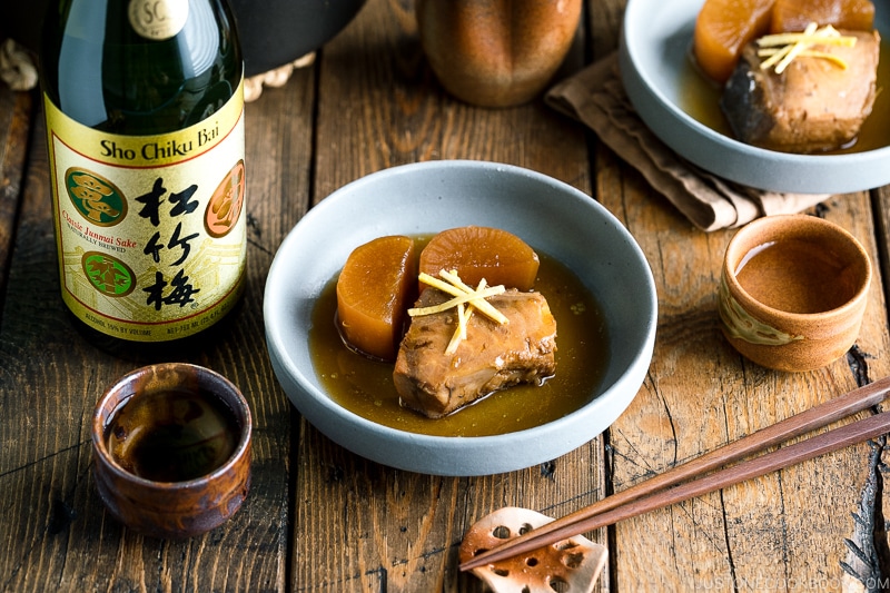 A grey bowl containing buri daikon, a simmered yellowtail and daikon radish, garnished with julienned ginger.