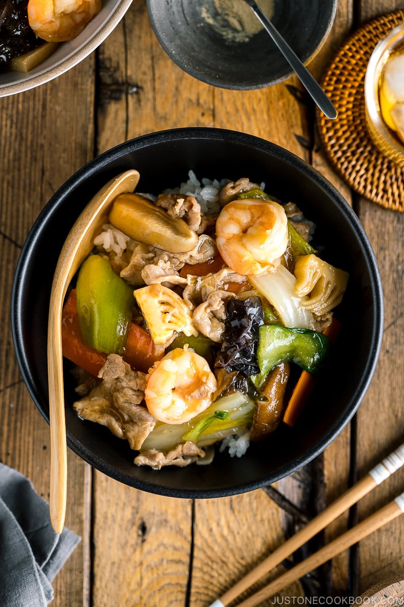A black bowl containing Chukadon (Seafood and Vegetable Stir Fry Over Rice).