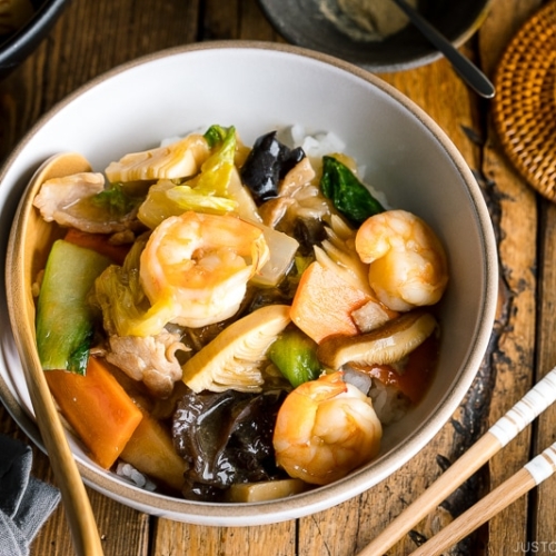 A white bowl containing Chukadon (Seafood and Vegetable Stir Fry Over Rice).