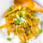 A white bowl containing pork curry over steamed rice.