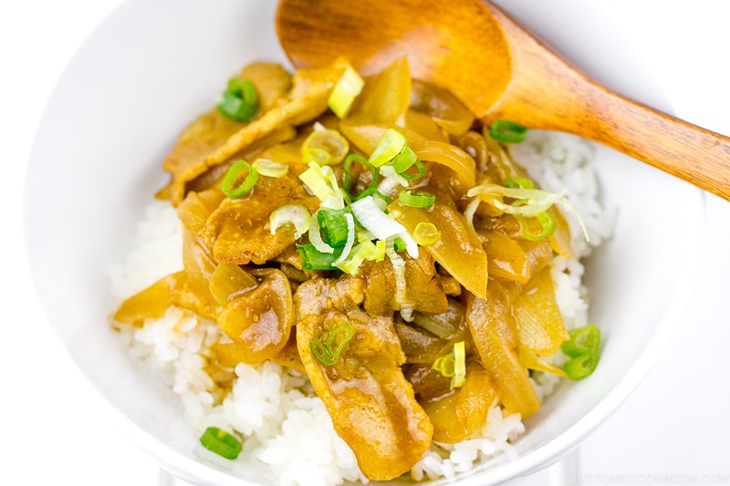 A white bowl containing pork curry over steamed rice.