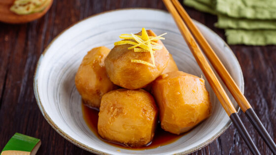 A white ceramic bowl containing simmered taro topped with julienned lemon zest.