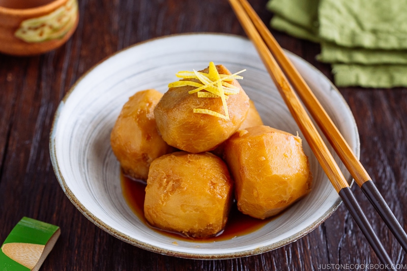 A white ceramic bowl containing simmered taro topped with julienned lemon zest.