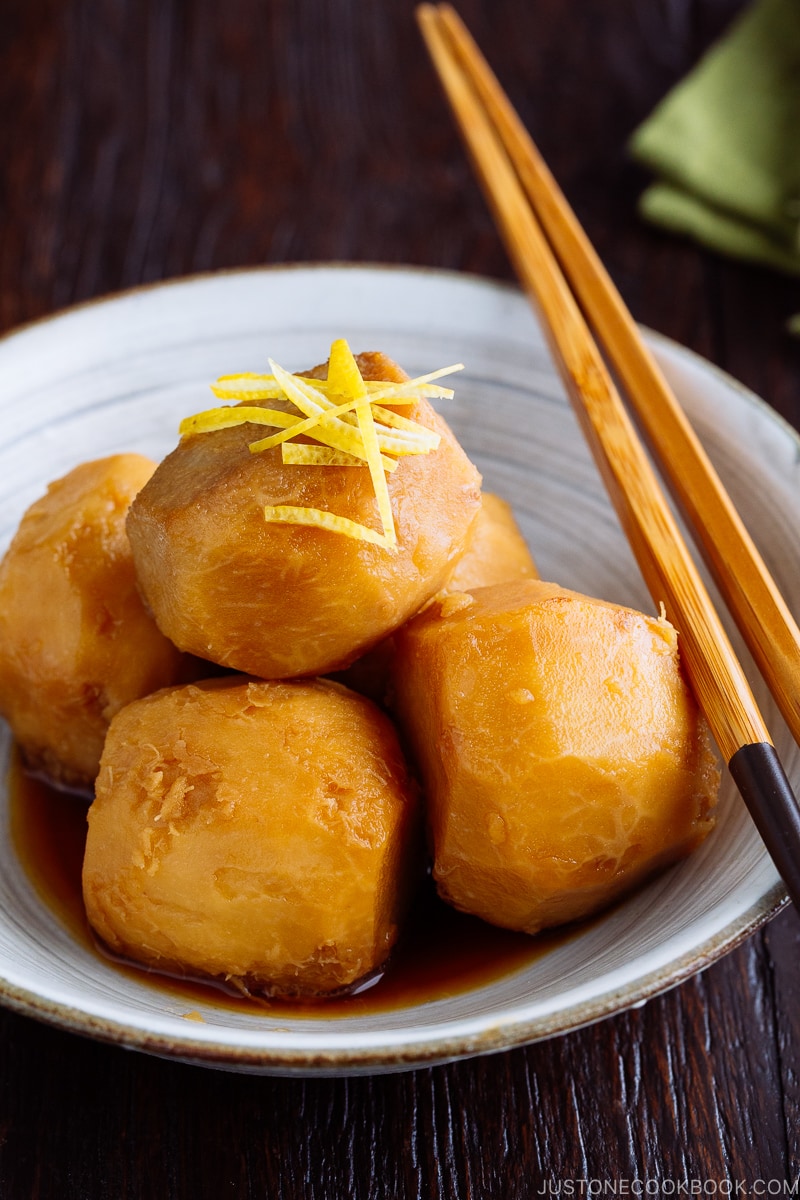 A white ceramic bowl containing simmered taro topped with julienned lemon zest.