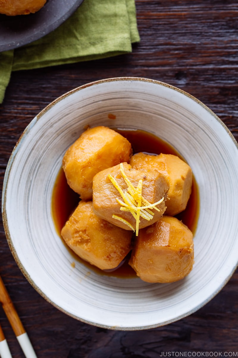 A white ceramic bowl containing simmered taro topped with julienned lemon zest.