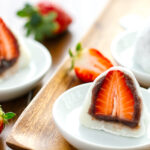 White plates containing strawberry mochi cut in half.