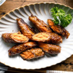 An oval ceramic plate containing Carrot Beef Rolls garnished with parley.