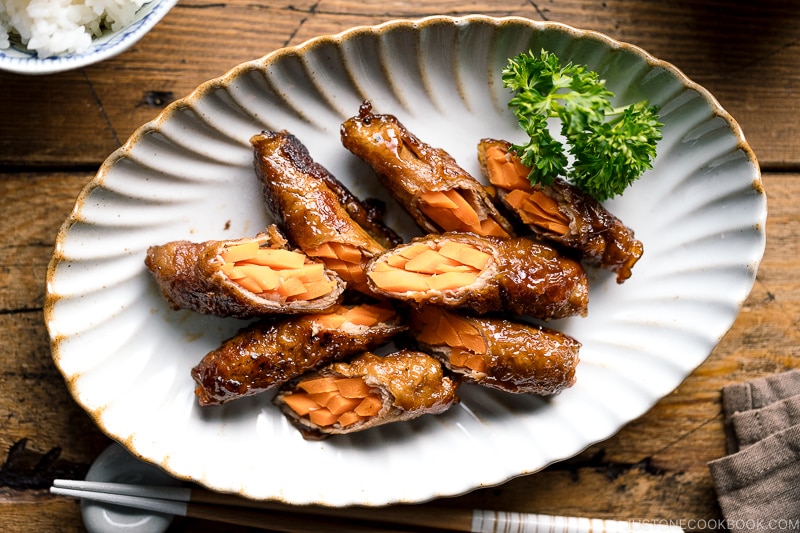 An oval ceramic plate containing Carrot Beef Rolls garnished with parley.