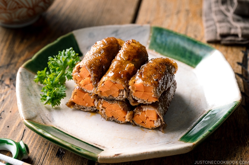 An oval ceramic plate containing Carrot Beef Rolls garnished with parley.