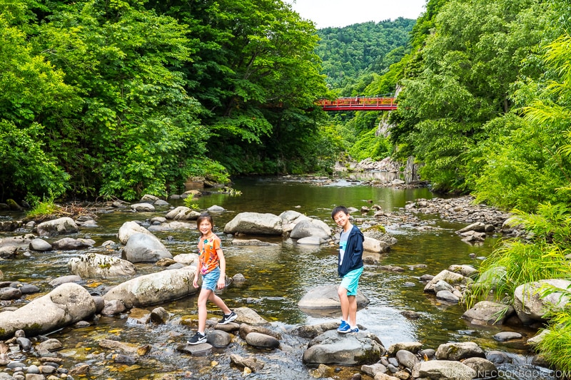 two children standing on rock on the Toyohira River with a bridge in the background