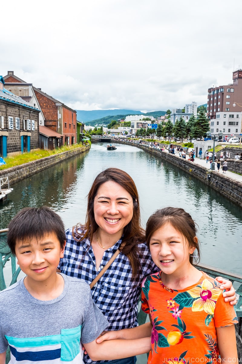 three people standing on a bridge on top of Otaru Canal