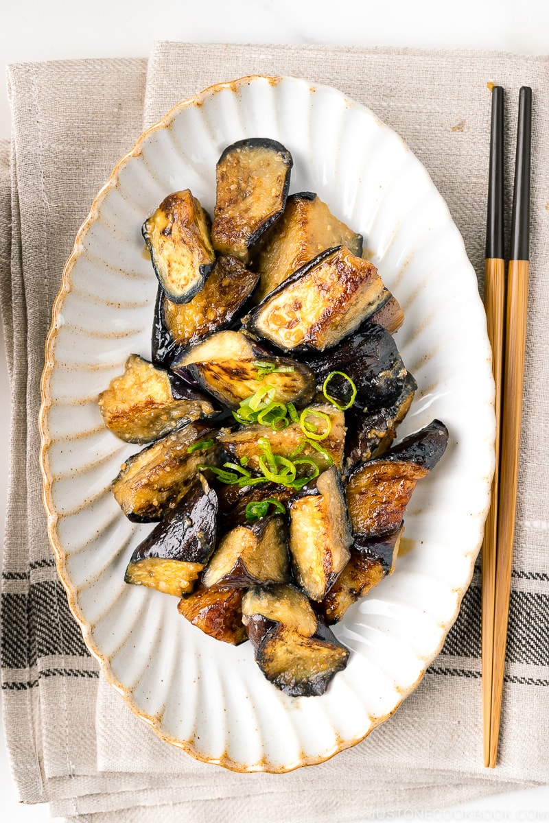 A white oval ceramic plate containing stir fry miso eggplant garnished with scallion.