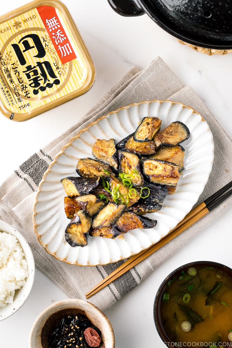 A white oval ceramic plate containing stir fry miso eggplant garnished with scallion.