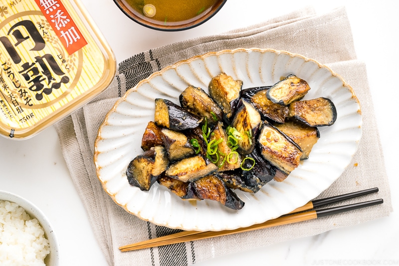 A white oval ceramic plate containing stir fry miso eggplant garnished with scallion.