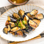 A white oval ceramic plate containing stir fry miso eggplant garnished with scallion.